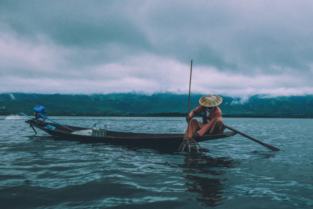 Fisherman in a small boat with mountains in the background and a cloudy sky